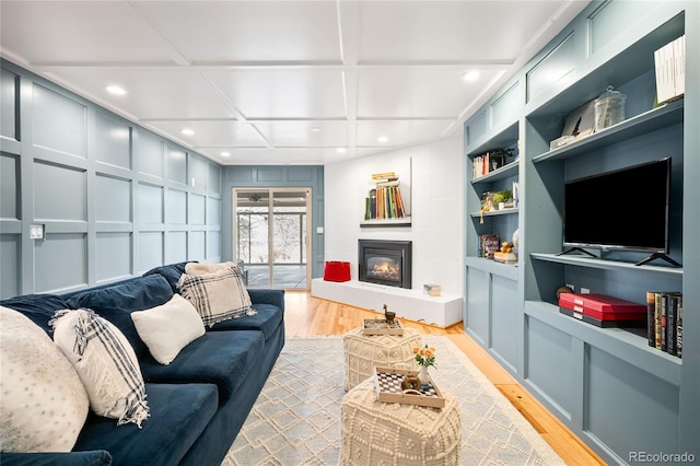 living area with light wood-type flooring, a glass covered fireplace, recessed lighting, built in shelves, and coffered ceiling