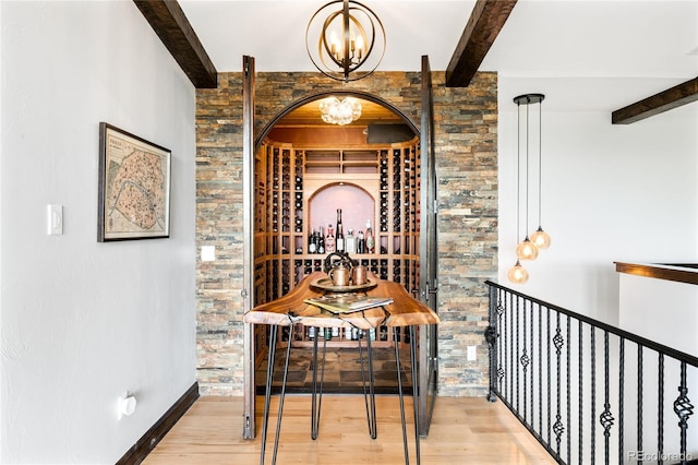 wine cellar featuring beamed ceiling, wood finished floors, baseboards, and an inviting chandelier