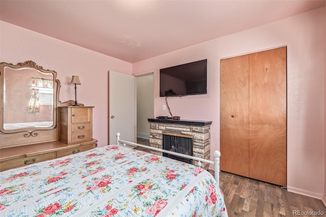 bedroom with a closet, a stone fireplace, and wood finished floors