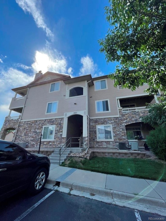 9557 W San Juan Cir Unit 207, Littleton, CO 80128 - view of front facade featuring stone siding, uncovered parking, and a chimney