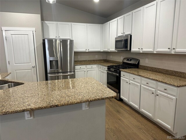 kitchen featuring white cabinetry, light stone countertops, vaulted ceiling, and stainless steel appliances