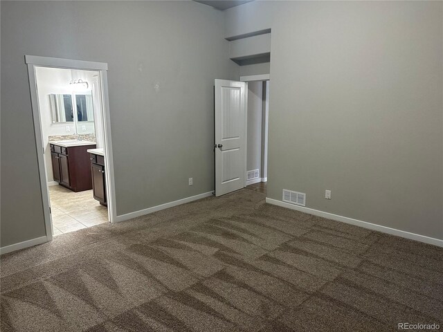 unfurnished bedroom featuring light carpet, ensuite bath, and sink