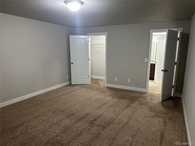 unfurnished bedroom featuring carpet floors, a textured ceiling, a spacious closet, and a closet