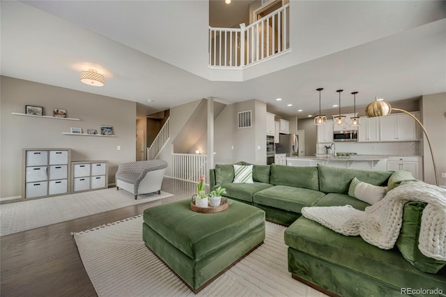 living area with stairs, recessed lighting, light wood-type flooring, a towering ceiling, and visible vents