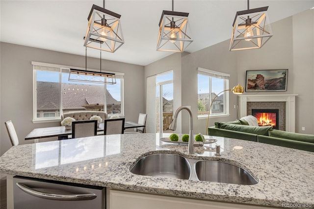 kitchen featuring a glass covered fireplace, light stone countertops, open floor plan, a sink, and dishwasher
