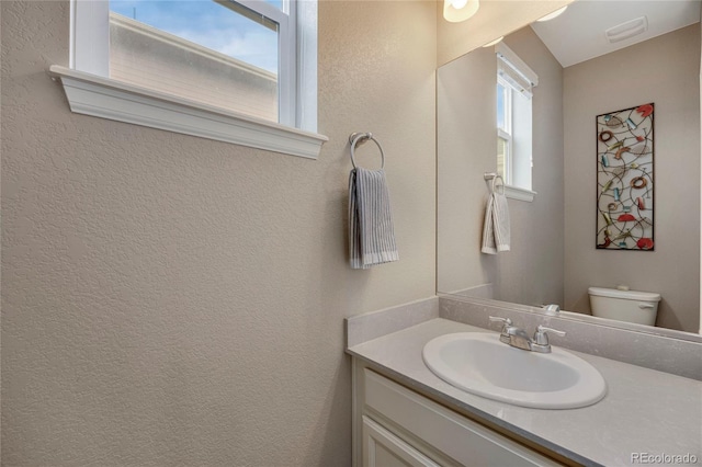 bathroom with vanity, a textured wall, toilet, and visible vents