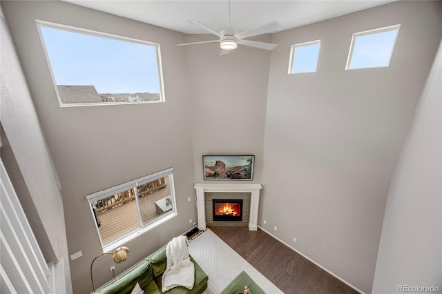 living area featuring ceiling fan, a high ceiling, a fireplace, baseboards, and wood finished floors