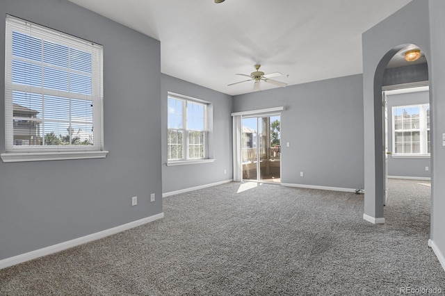 carpeted spare room featuring arched walkways, a ceiling fan, and baseboards