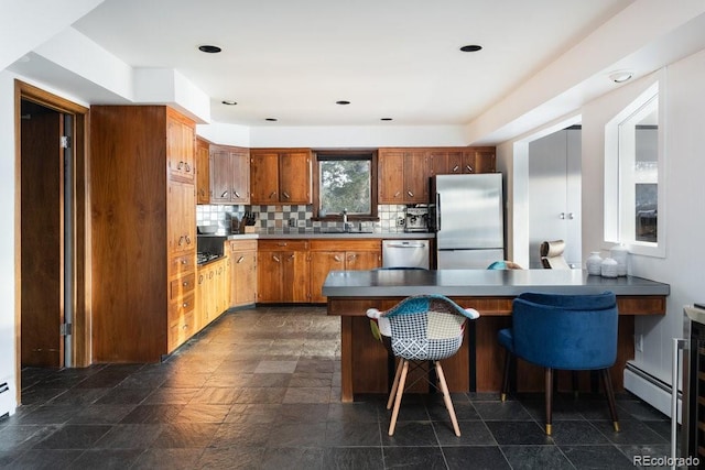 kitchen featuring a kitchen bar, sink, baseboard heating, appliances with stainless steel finishes, and backsplash