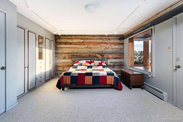 carpeted bedroom featuring a baseboard heating unit, track lighting, and wood walls