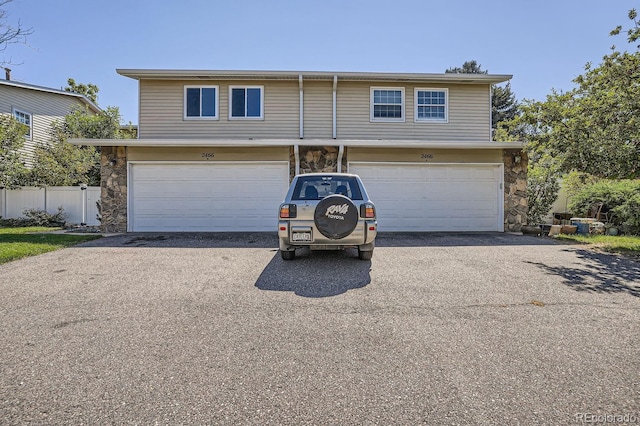 view of front of property with aphalt driveway, stone siding, an attached garage, and fence