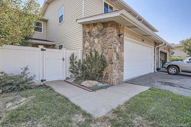 view of property exterior featuring driveway, a gate, stone siding, fence, and a garage