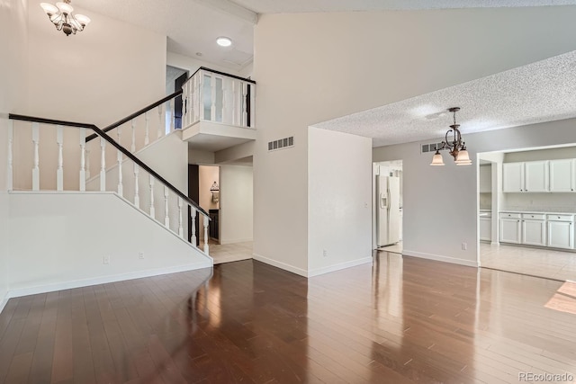 unfurnished living room featuring wood-type flooring, a textured ceiling, a towering ceiling, and a chandelier