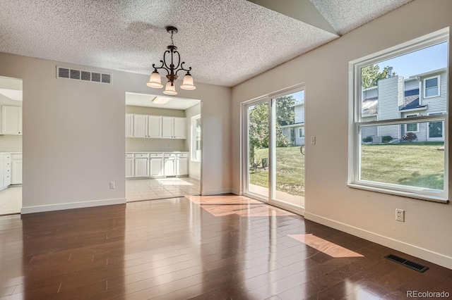 unfurnished dining area featuring wood-type flooring, an inviting chandelier, and a textured ceiling