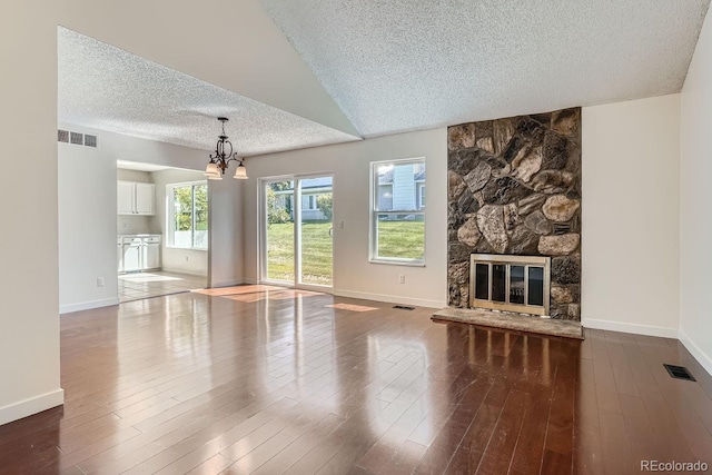 unfurnished living room featuring wood-type flooring, a stone fireplace, a textured ceiling, and a notable chandelier