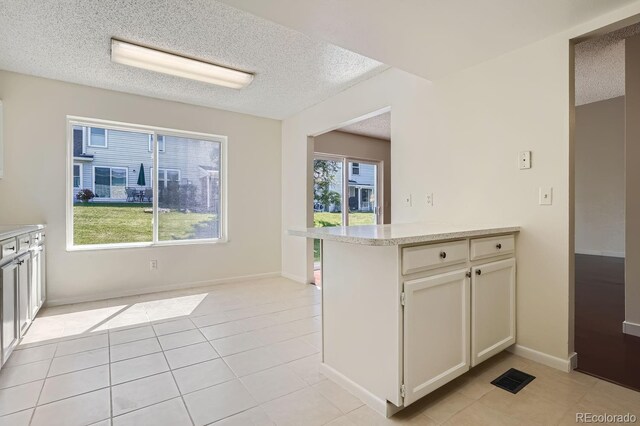 kitchen featuring a healthy amount of sunlight, kitchen peninsula, light tile patterned floors, and white cabinets