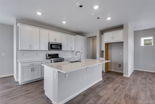 kitchen featuring sink, appliances with stainless steel finishes, white cabinetry, a center island with sink, and decorative backsplash