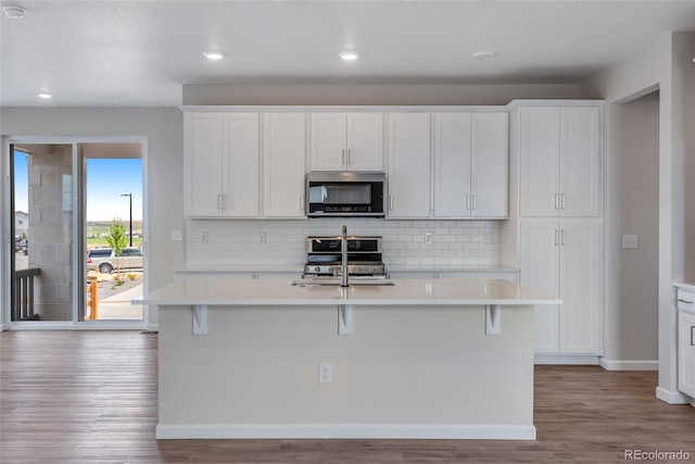 kitchen with appliances with stainless steel finishes, tasteful backsplash, white cabinets, a kitchen bar, and a center island with sink