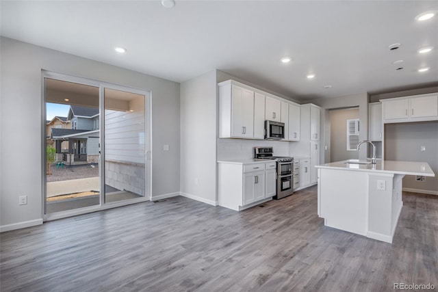 kitchen with appliances with stainless steel finishes, sink, white cabinets, light hardwood / wood-style floors, and a center island with sink