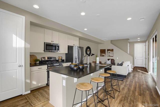 kitchen with stainless steel appliances, white cabinetry, a center island with sink, and a kitchen bar