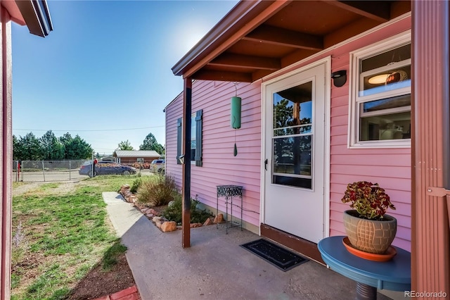 property entrance with a patio area, fence, and a lawn