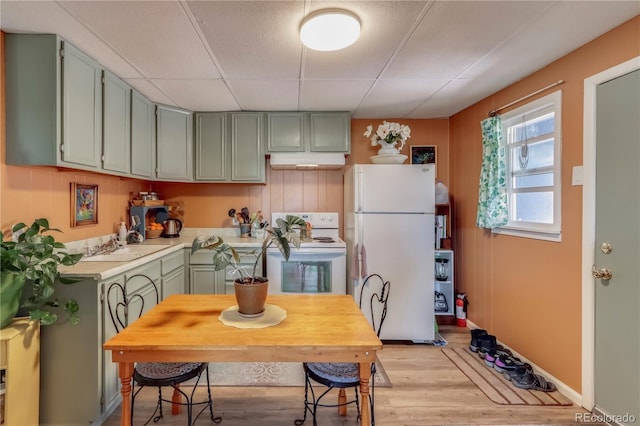 kitchen with a sink, light countertops, light wood-type flooring, white appliances, and under cabinet range hood