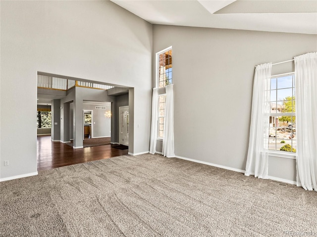 unfurnished living room featuring high vaulted ceiling and dark carpet