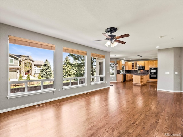 unfurnished living room with ceiling fan with notable chandelier and dark hardwood / wood-style flooring