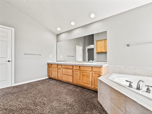 bathroom with vanity, tiled tub, vaulted ceiling, and a textured ceiling