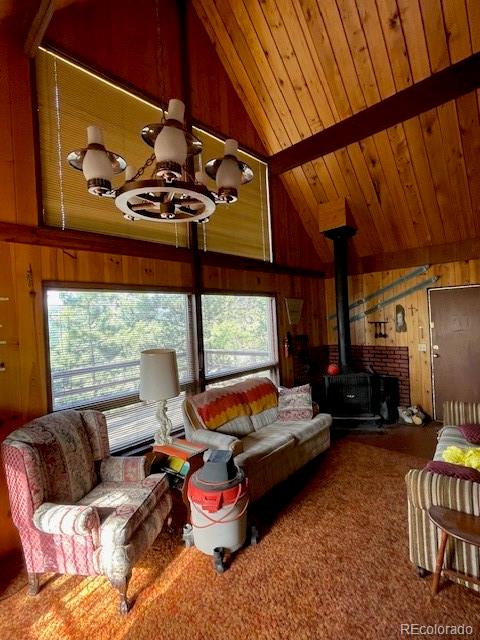 living room featuring wood ceiling, high vaulted ceiling, an inviting chandelier, and a wood stove