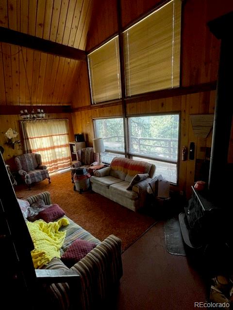 living room featuring carpet floors, high vaulted ceiling, wooden ceiling, and wooden walls