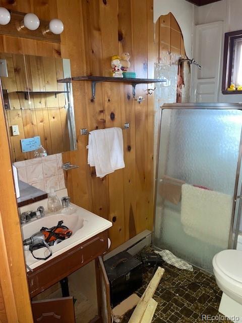 bathroom featuring sink, toilet, wooden walls, and an enclosed shower