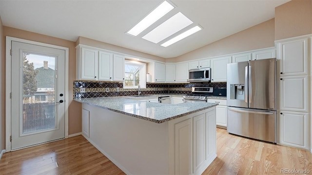 kitchen featuring kitchen peninsula, appliances with stainless steel finishes, light stone counters, lofted ceiling with skylight, and white cabinets