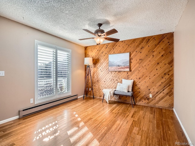 unfurnished room featuring wooden walls, a textured ceiling, hardwood / wood-style floors, ceiling fan, and baseboard heating