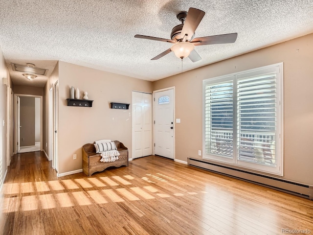 unfurnished room with ceiling fan, baseboard heating, light hardwood / wood-style flooring, and a textured ceiling