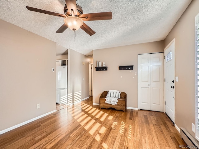 unfurnished room with light wood-type flooring, ceiling fan, a baseboard radiator, and a textured ceiling