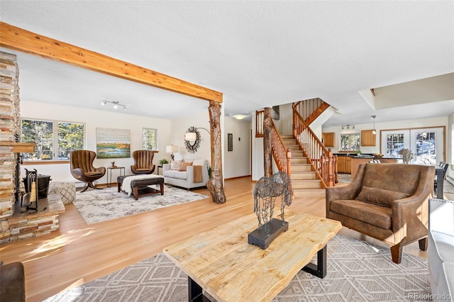 living area with beamed ceiling, a textured ceiling, stairs, and light wood-style floors