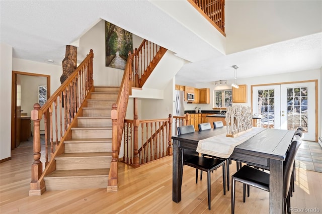 dining space featuring light wood-type flooring, a high ceiling, stairway, and french doors