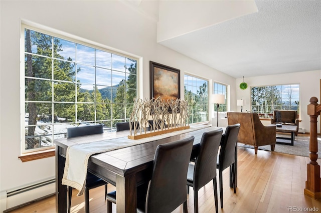 dining room featuring a baseboard heating unit, light wood-style flooring, and a textured ceiling