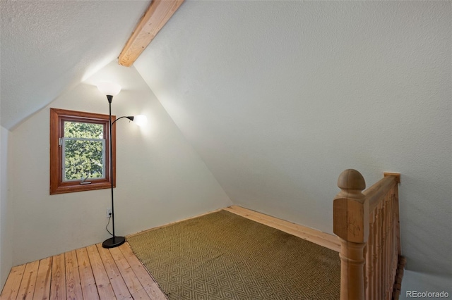 additional living space featuring wood-type flooring and vaulted ceiling with beams