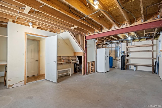 unfinished below grade area featuring electric panel and freestanding refrigerator