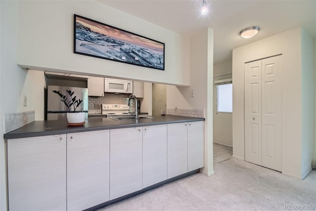 kitchen with sink, stainless steel refrigerator, white cabinetry, light carpet, and decorative backsplash