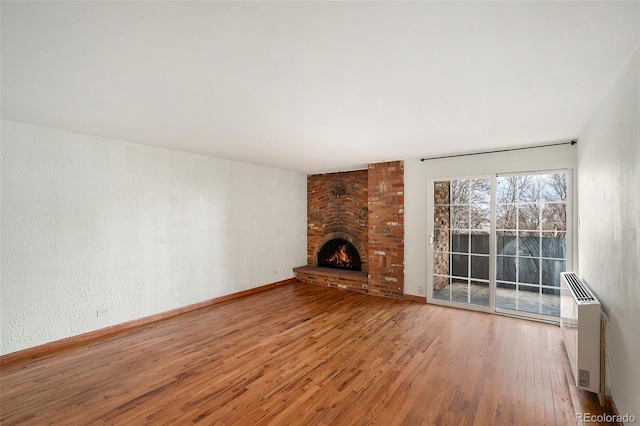 unfurnished living room with a brick fireplace, heating unit, and hardwood / wood-style floors