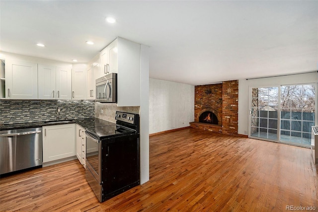 kitchen with appliances with stainless steel finishes, a fireplace, light wood-type flooring, and white cabinets