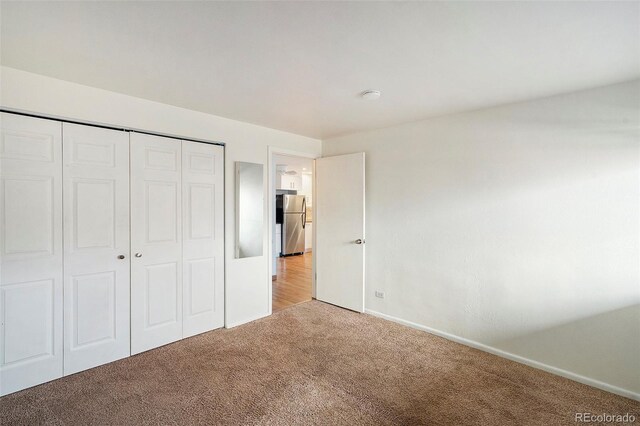 unfurnished bedroom featuring stainless steel fridge, light colored carpet, and a closet