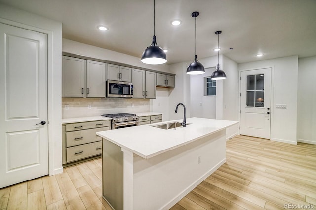 kitchen featuring decorative backsplash, appliances with stainless steel finishes, gray cabinets, light wood-style floors, and a sink