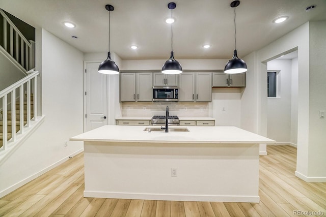 kitchen featuring gray cabinetry, stainless steel appliances, a sink, light wood-type flooring, and decorative backsplash