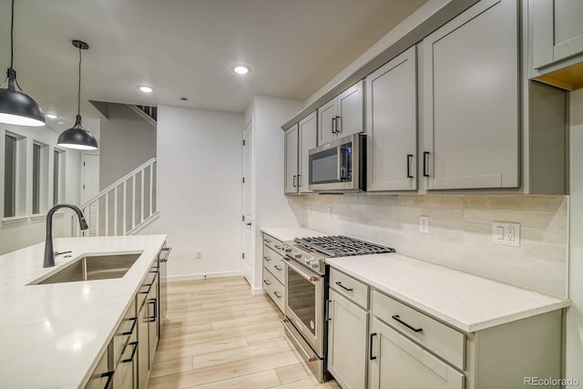 kitchen with a sink, light wood-style floors, appliances with stainless steel finishes, backsplash, and light stone countertops