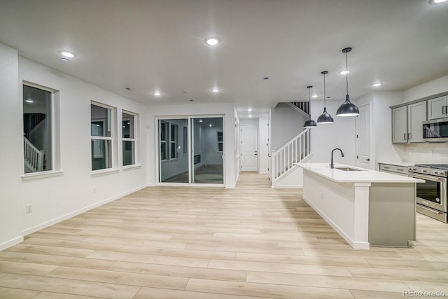 kitchen featuring stainless steel appliances, a sink, light countertops, light wood finished floors, and an island with sink