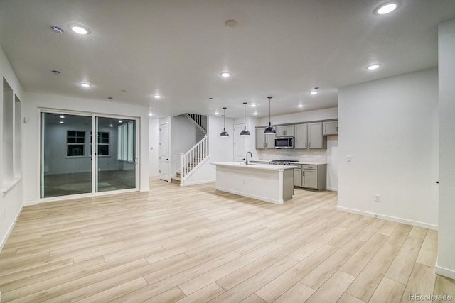 kitchen with open floor plan, gray cabinets, light wood finished floors, stainless steel microwave, and an island with sink